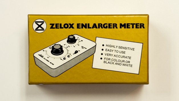 Photograph of a vintage box for an enlarger meter with black and white illustration showing the product against a gold background