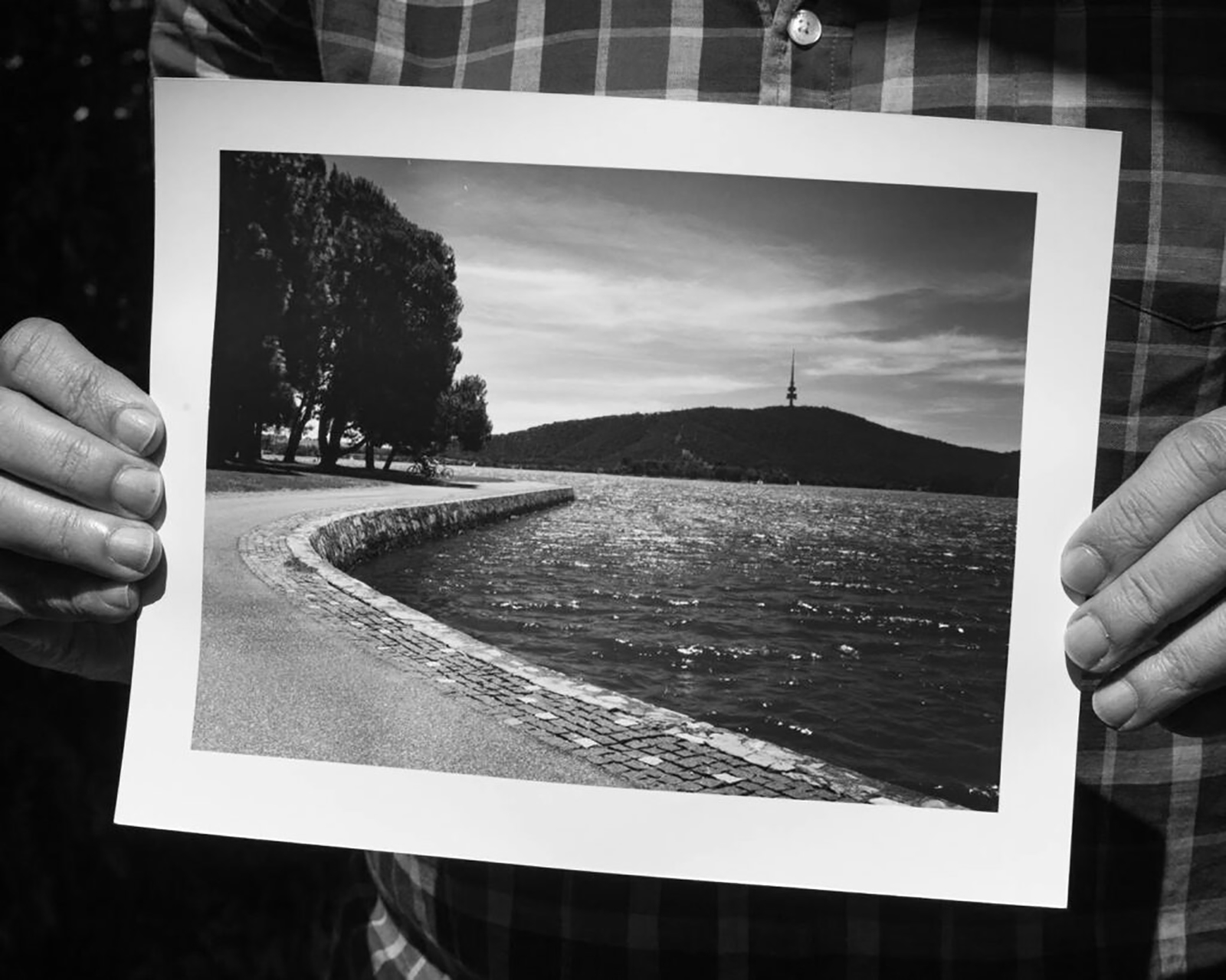 An image of hands holding up a black and white photograph of Lake Burley Griffin in Canberra