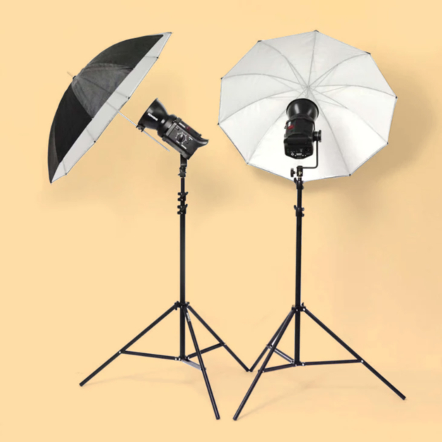 Photograph of two studio lights on tripods and with light diffusing umbrellas attached against a warm yellow background.