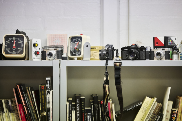 Photograph of a collection of old vintage cameras on top of a bookshelf in natural daylight