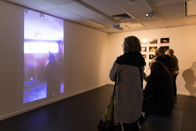 A photograph of two people viewing a video work at an exhibition in a gallery