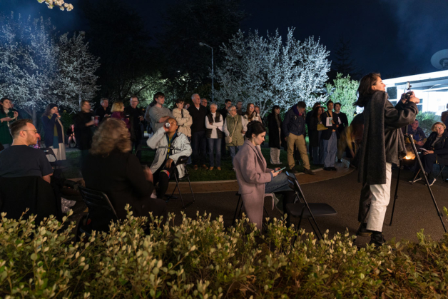 Photograph shot at night with flash showing a crowd gathered outside with trees in the background lit up in blue and green