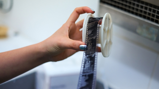 A photograph of a hand removing film off of a reel after its been developed