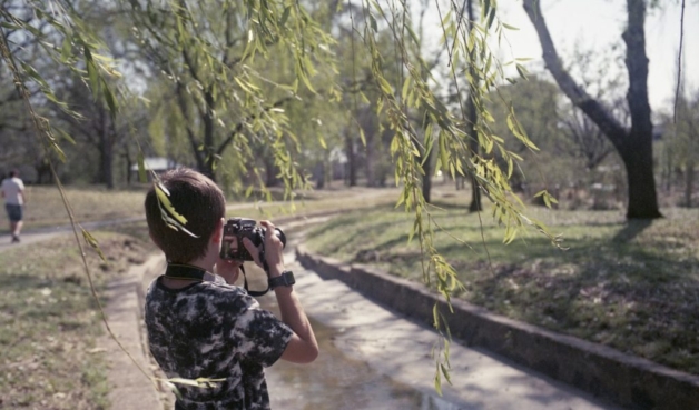 A photograph of a boy holding a camera taking a photograph of a tree