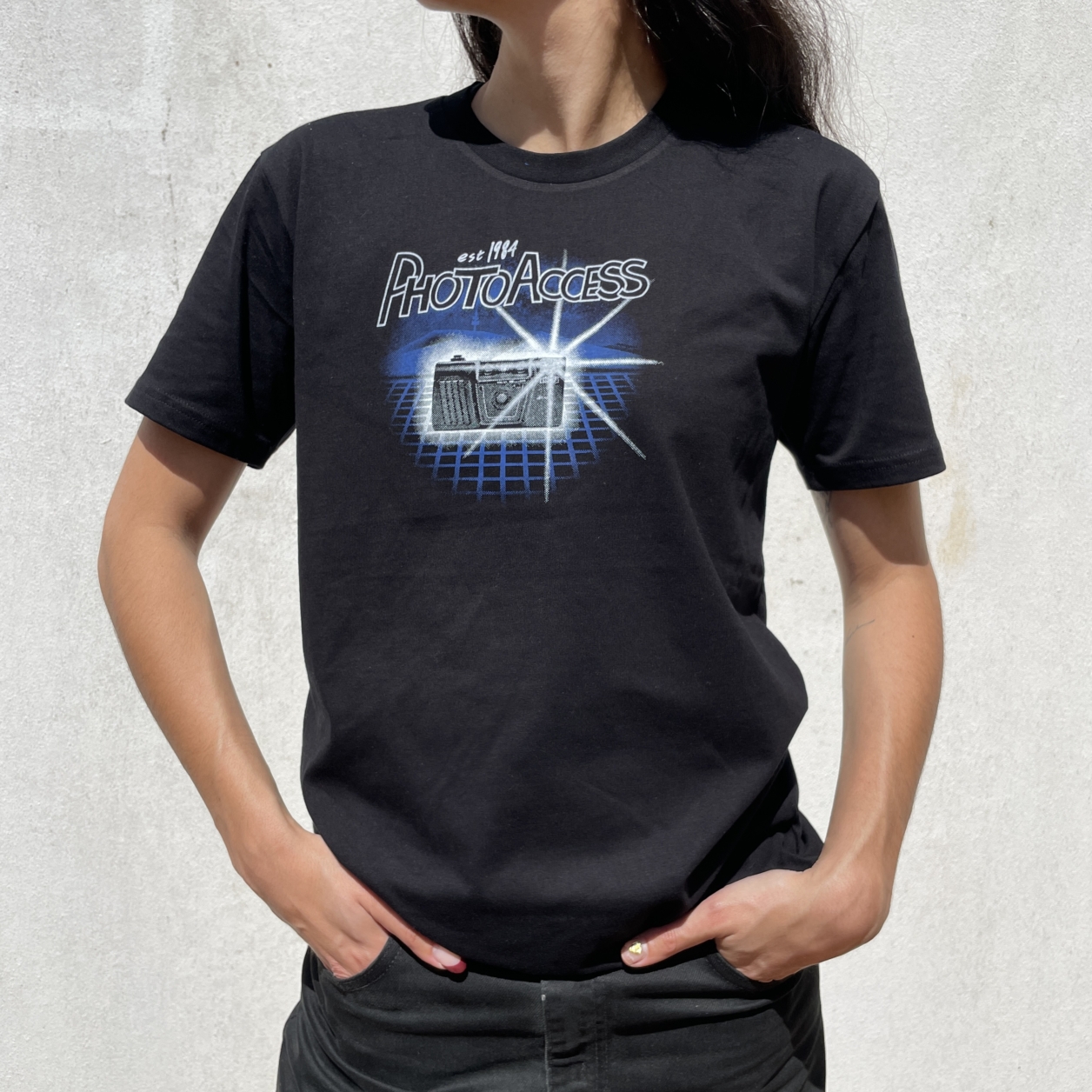 An image of a woman wearing a black t-shirt with a camera graphic with a bright flash, and 'PhotoAccess' logo on top