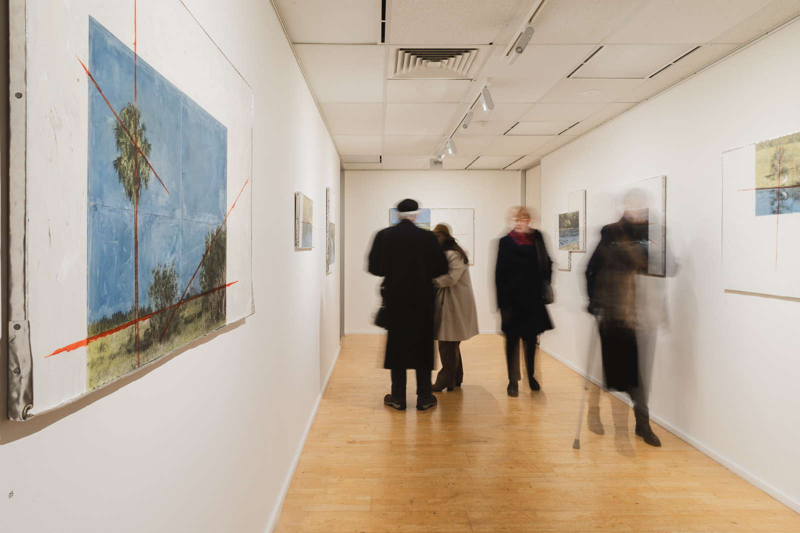 An image of a gallery with artwork on the walls and people walking around viewing the art.