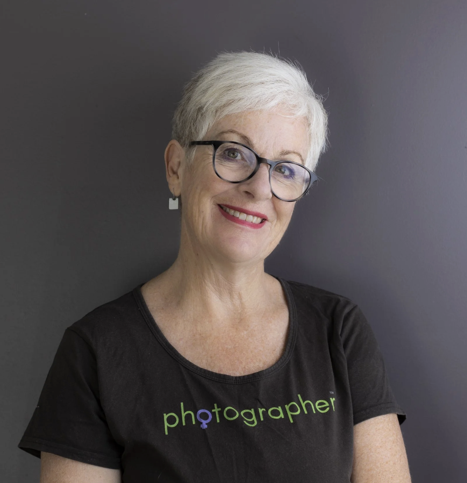 An image of a woman with short white hair wearing glasses smiling