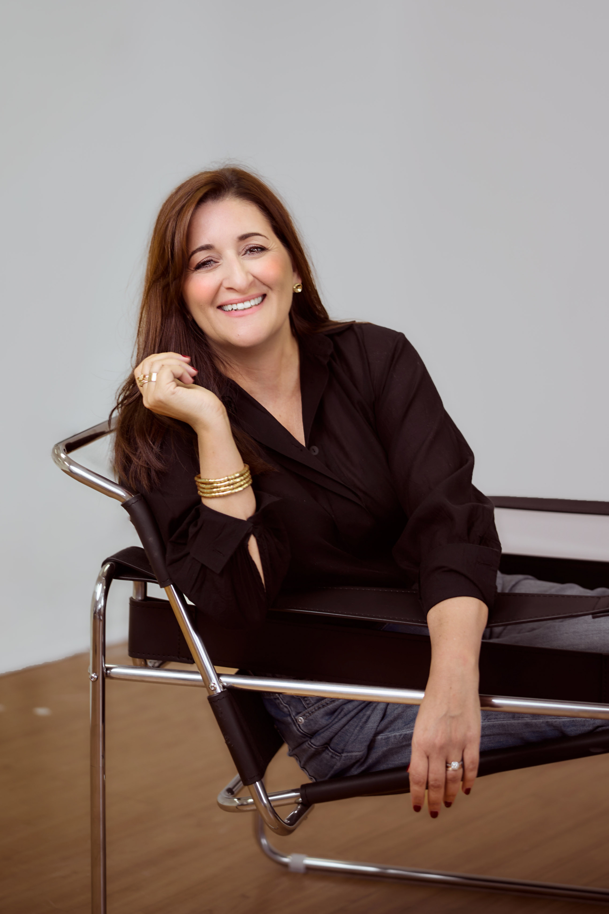 A photograph of a woman with brown hair and brown eyes smiling at the camera, leaning back in a black leather chair