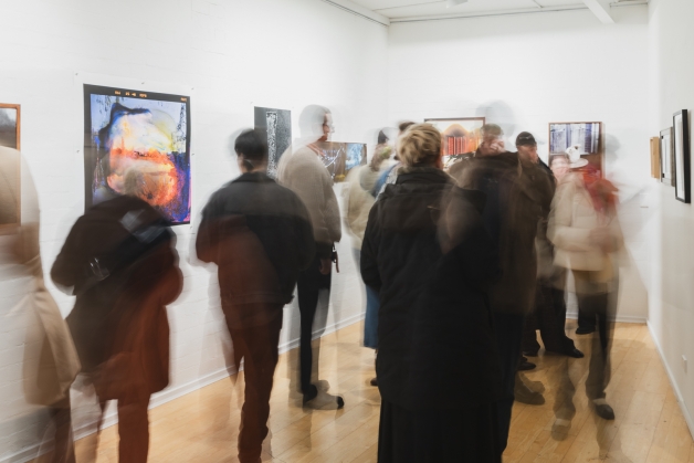 A photograph of many people in a gallery space with photographs on the walls